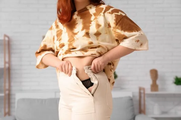 Image of woman trying to do her trousers up after pregnancy weight gain Livingston