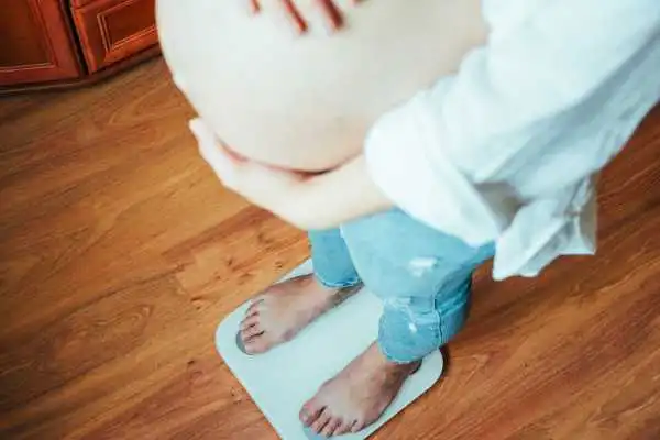 Image of woman weighing herself and experiencing weight gain through pregnancy Livingston